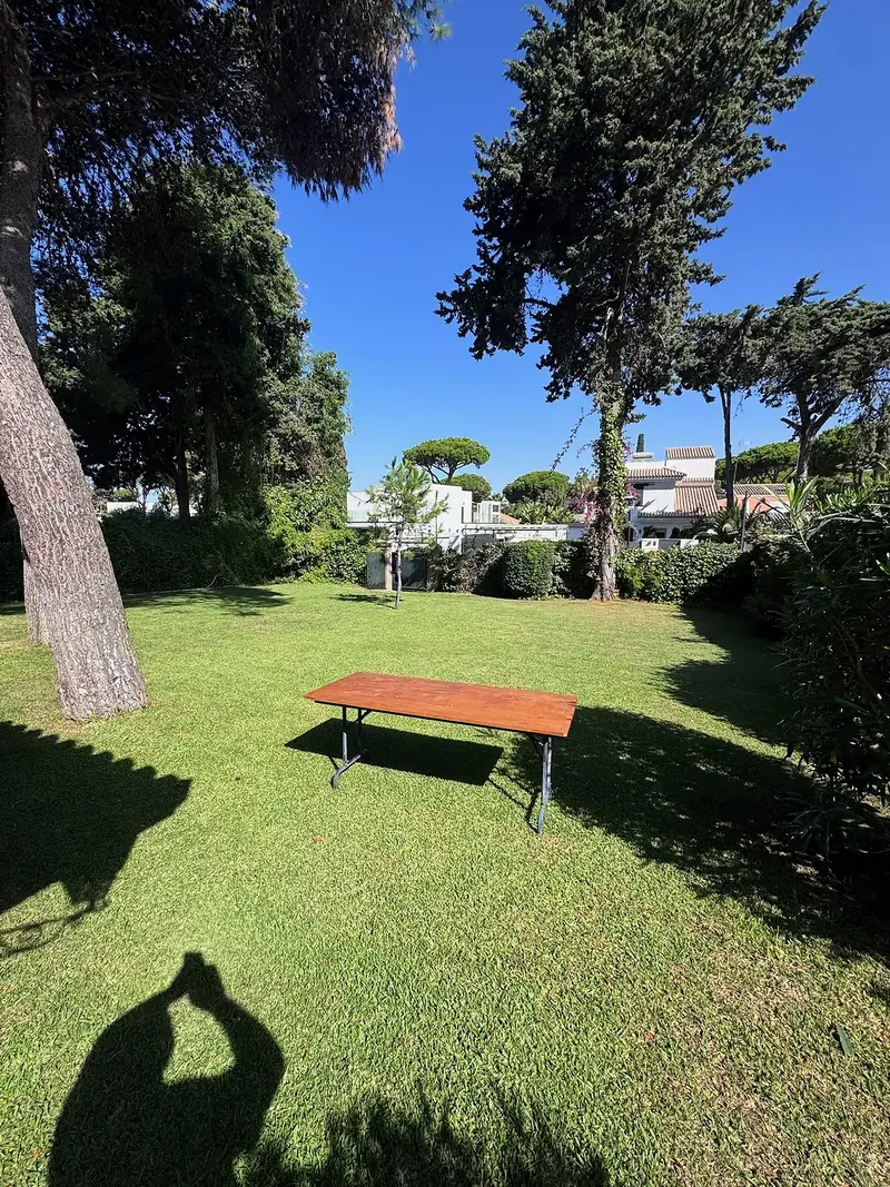 Rincón de sombra con banco bajo pinos piñoneros en un jardín de El Puerto