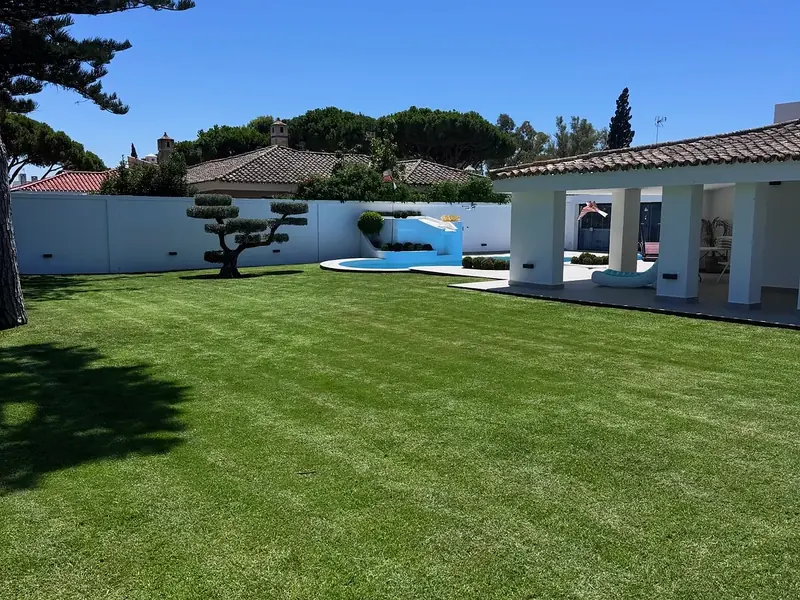 Jardín de diseño con césped rayado, topiario en nube, piscina y porche en un chalet de Vistahermosa